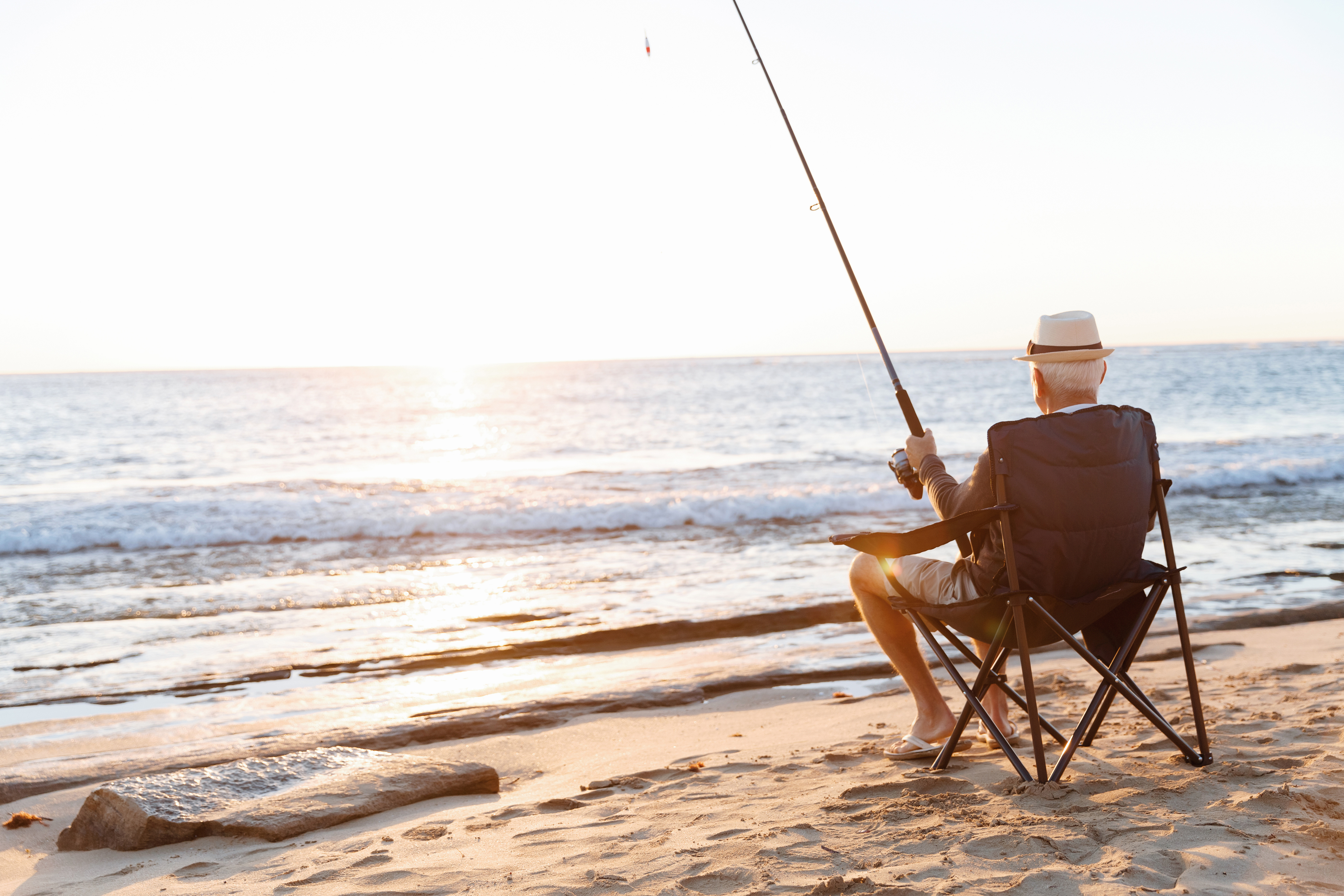 Ein älterer Herr genießt die Rente angelnd am Strand